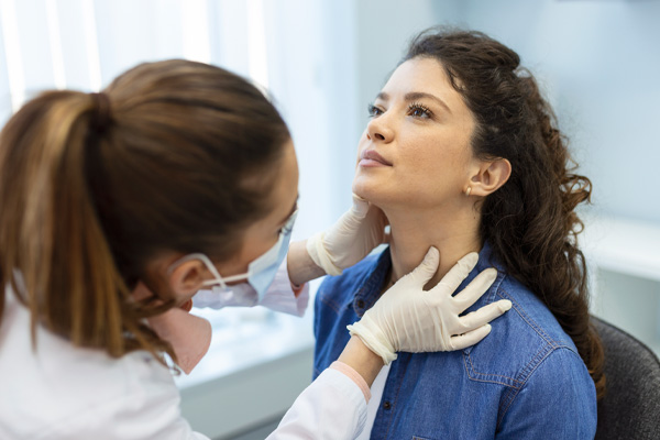 endocrinologist examining the throat of a young woman in a doctor’s office