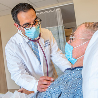doctor saadat listening to a patient's heartbeat in hospital bed