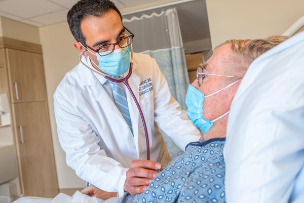 doctor saadat listening to a patient's heartbeat in hospital bed