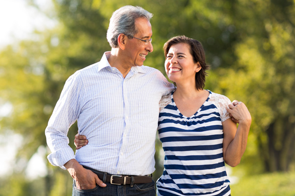 An older couple taking a walk in nature, arms around each other, smiling at each other