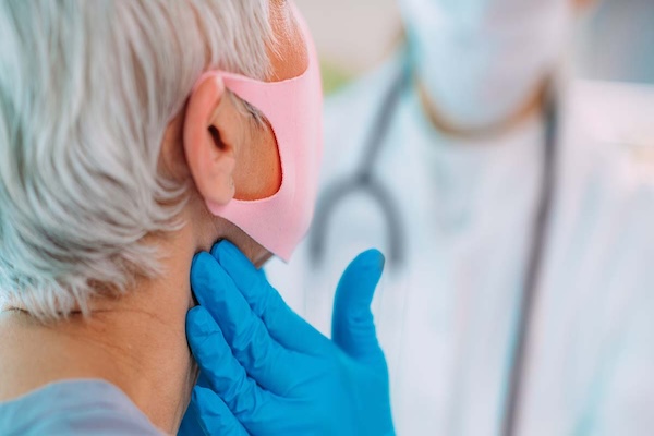 a masked doctor checks a woman's thyroid