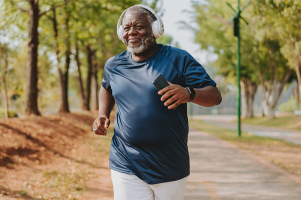 an older Black man jogging in a park wearing headphones