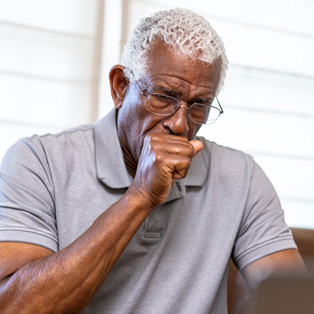 Man on couch coughing into clenched fist