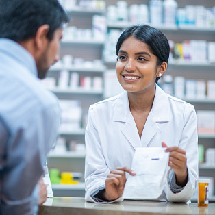 Woman pharmacist behind pharmacy counter, providing male patient with their medication.
