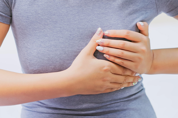 a woman in a gray tshirt holding her left breast as if in pain
