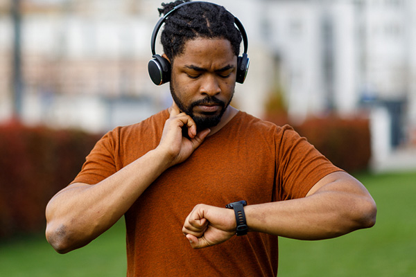 a Black man in running clothes and headphones checking his heart rate on a smartwatch