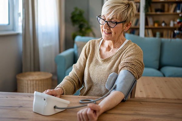 an older woman with short hair and glasses checking her blood pressure at home