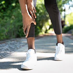 a woman's legs from the knees down, wearing athletic clothes and shoes, her hands on her calf in pain