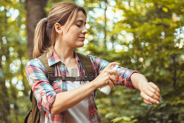 a woman on a hike protecting herself from mosquitoes with bug spray and clothing