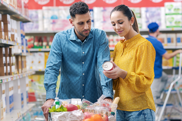 a man in a long-sleeved blue shirt and a woman in a bright yellow shirt reading nutrition labels in the grocery store aisle