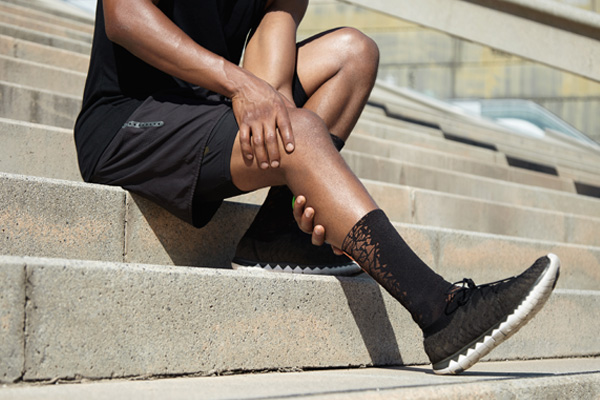 a runner holding his extended leg in discomfort while sitting on a staircase