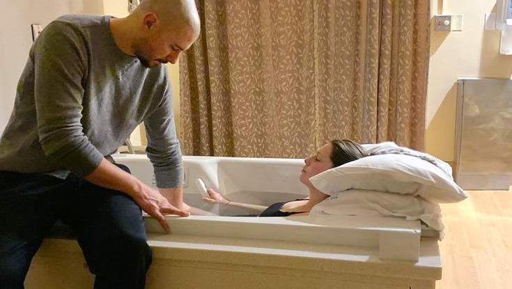 a woman in a birthing tub being assisted by her partner in having a water birth
