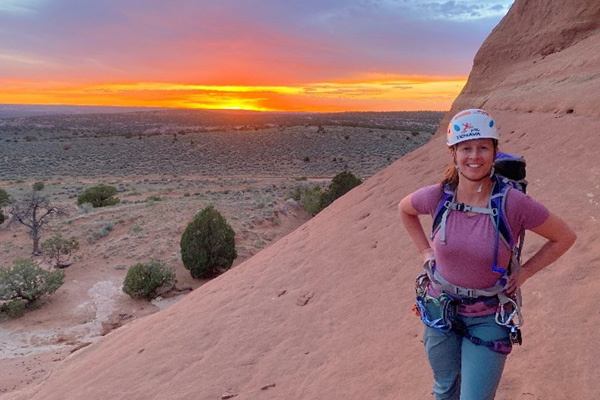 Leah Manchester, MD hiking in a helmet posed in front of a sunset