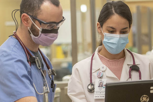 Candid photo of two emergency room residents in scrubs standing around a computer in the hospital