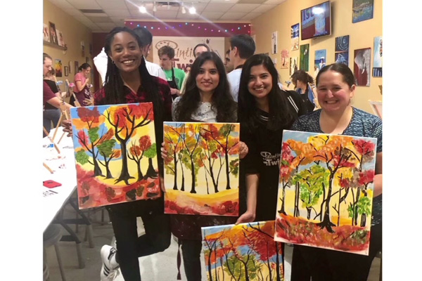 four internal medicine residents holding up their paintings at a paint night