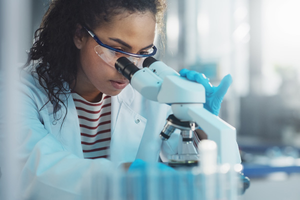 a woman scientist in a lab coat stares into a microscope