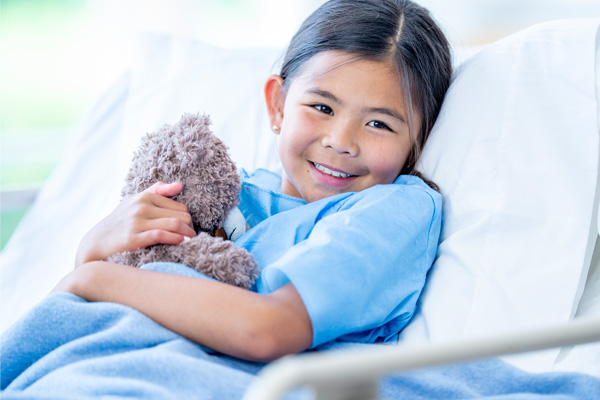 a smiling child in a hospital bed holding a teddy bear