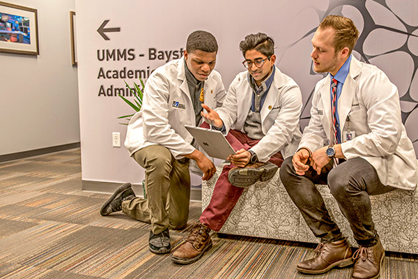 four medical students looking at a tablet in their white coats