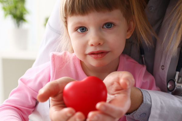 a child and hands of a doctor holding a small plastic heart