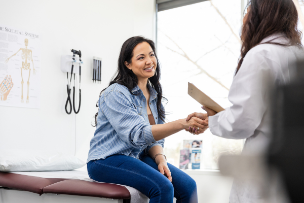 A woman in a blue shirt with brown hair shakes the hand of a doctor in an emergency department setting.
