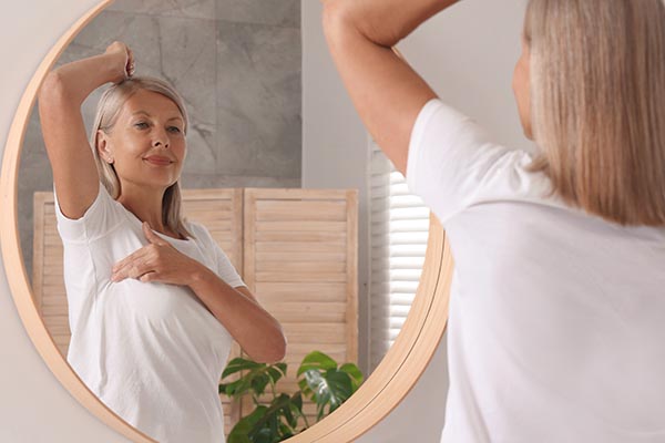 a woman in a plain white tshirt conducting a breast self exam in a mirror