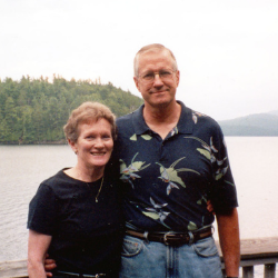 Millie and Ronald Burkman stand outdoors with a tree covered island behind them