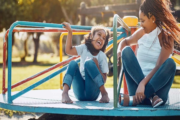 a mother and daughter at the park riding a spinning carousel 