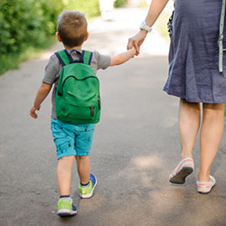 mother and child with backpack holding hands walking to school