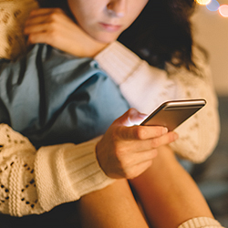 Woman looking at phone while hunched over, holding on to blanket 