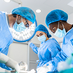 3 masked physicians looking down, preforming procedure