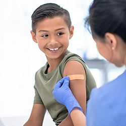 Child smiles at healthcare provider while they place band-aid on child's arm.
