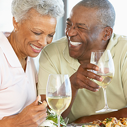An older Black couple enjoying some glasses of wine with dinner, laughing together