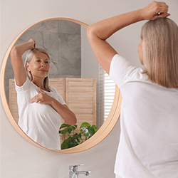 a woman in a plain white tshirt conducting a breast self exam in a mirror