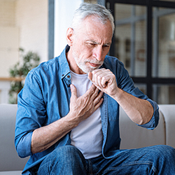 A man sitting down with shortness of breath and coughing