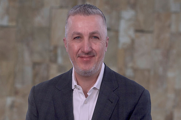 a man in a white collared shirt and sport coat smiling for the camera