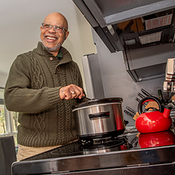 Dr. Frank Robinson, smiling at camera while stirring crockpot contents on stove.