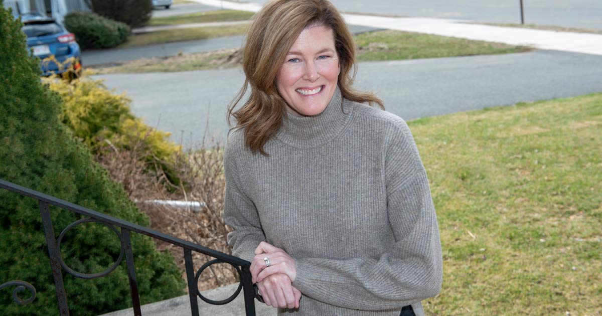 Shannon Schultz smiling with one hand on top of other, leaning on outdoor step railing