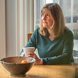 Susan holding a mug in hands while sitting at table and looking outside