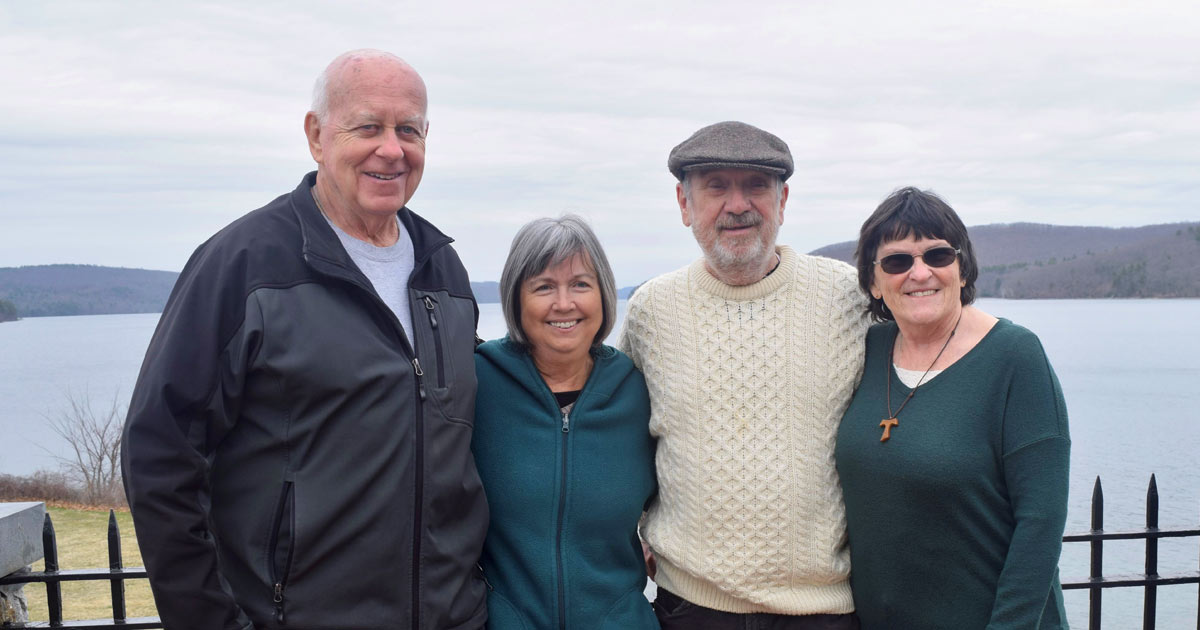 Terry & Barbara at Quabbin Reservoir with their spouses, smiling and standing in front of black fence