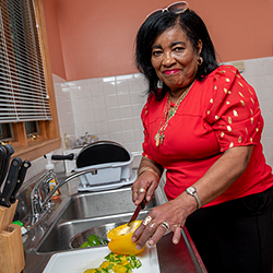 Yvonne Scott smiling with mouth closed while chopping peppers in kitchen