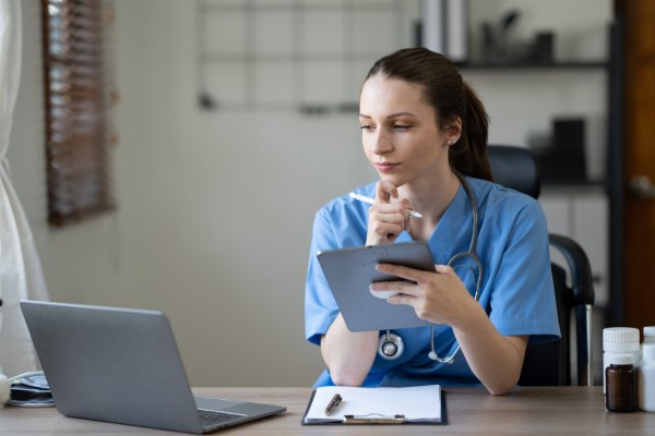 Doctor looks at laptop while holding a tablet