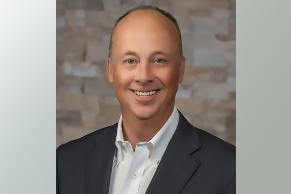 a man wearing a white button-down shirt and dark suit jacket smiling for the camera