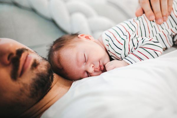 A close-up of baby boy sleeping on his father’s chest.
