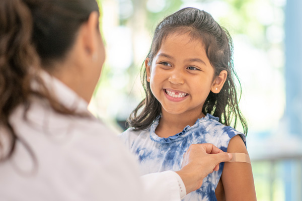 A female doctor places a small bandage on a young girl’s arm after giving her an immunization.