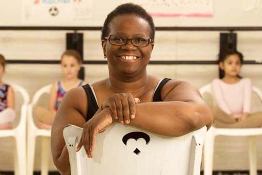 a dance teacher smiling with child dancers behind her