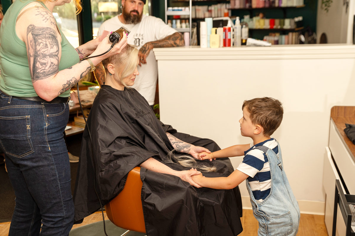 Jenn Venn holding her son's hands as a hairdresser shaves her head to a salon