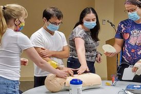 CPR class students placing their hand on the chest of test dummy.
