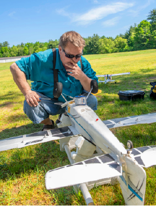 Man outside, crouched down to examine a model airplane.