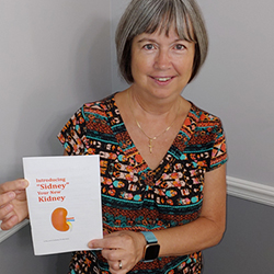 Barbara smiling while holding up “Introducing Sidney, your new kidney” book