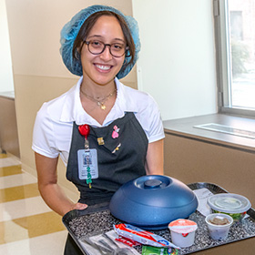 guest service employee smiling with a tray of hospital food